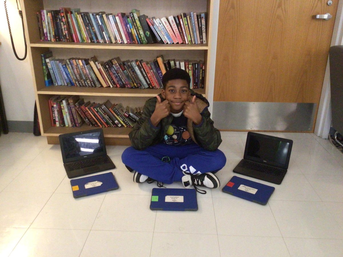 Here's a student smiling and giving a thumbs up while siting around computers and IPads.