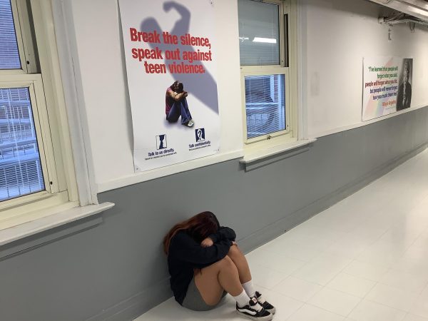 A student sits in a ball on the floor in front of antibullying poster.