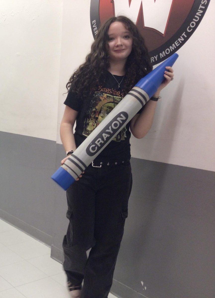 Mia poses with a giant crayon behind the WMS logo.