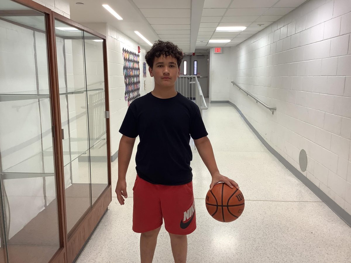 7th grader Jacob Flores holds a basketball while he stands in front of the shelves by the gymnasium doors on Monday at WMS