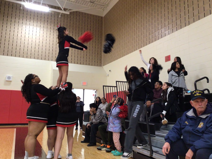 Cheerleaders perform a basketball stunt where the crowd throws pompoms at their arms to imitate the basketball players at WMS.