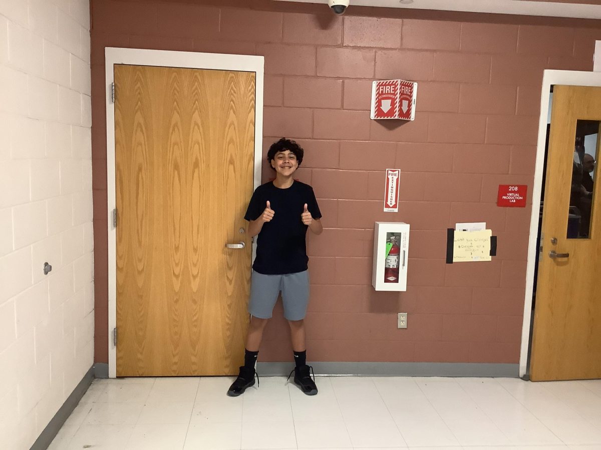 Aiden Collado poses outside room 208 for a picture
