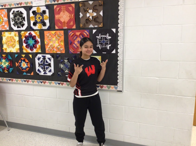 Olivia Sanchez, 7th grader,  poses in front of a bulletin board outside of the gym.