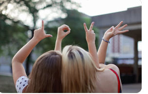Two friends using hand gestures to spell the word "love," indicating they're good friends, and care for one another.